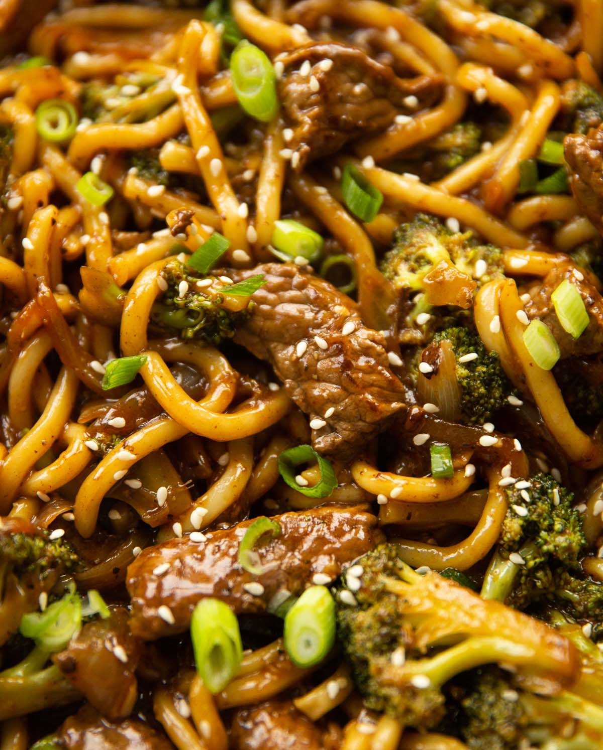 close up shot of beef and broccoli noodles in skillet garnished with sesame seeds and spring onion