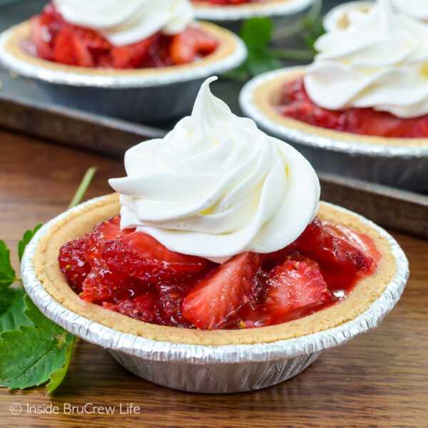 A mini strawberry pie in a graham cracker crust on a table with more pies behind it