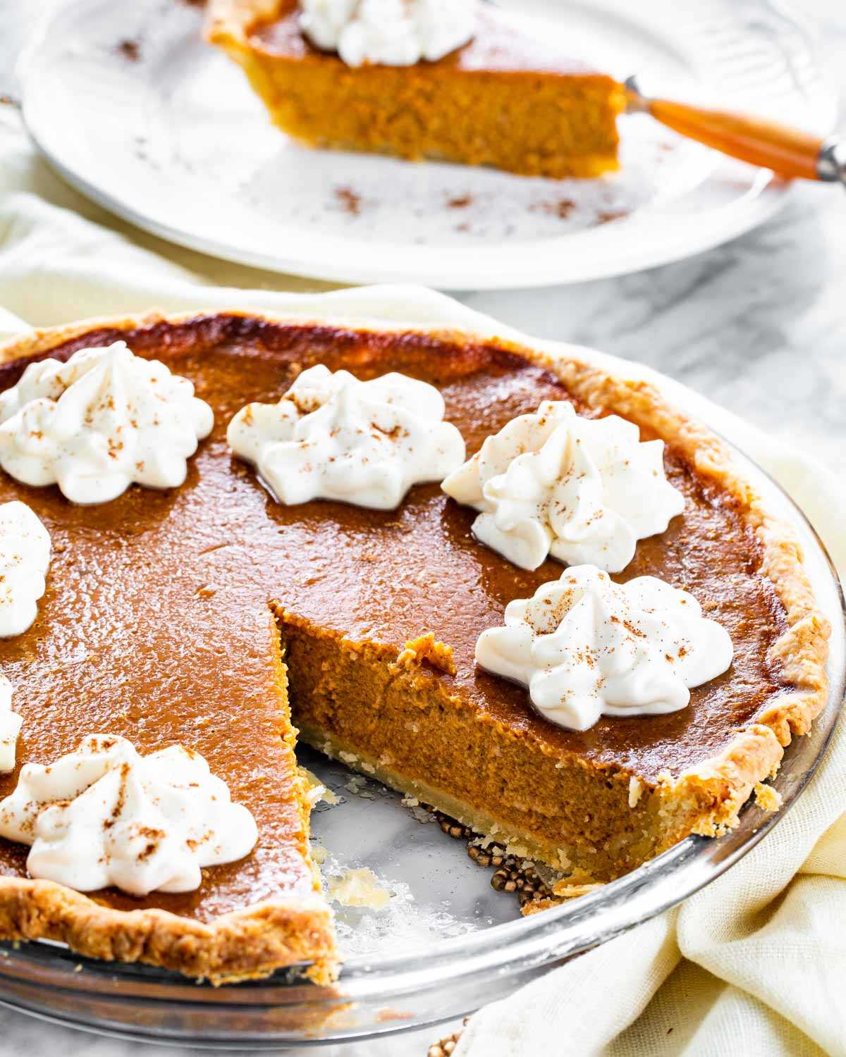 pumpkin pie topped with whipped cream with a slice on a plate in the background.
