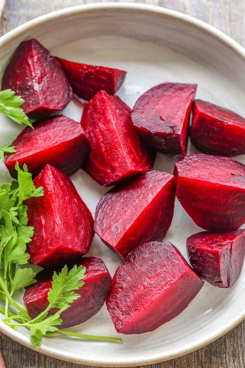 A white plate of cooked sliced beets with a bunch of greens.